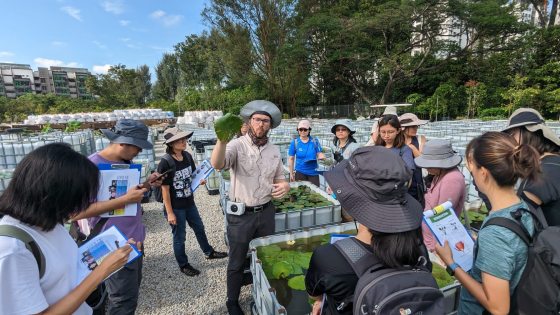 A group of people standing around a person holding a water lily leaf. 